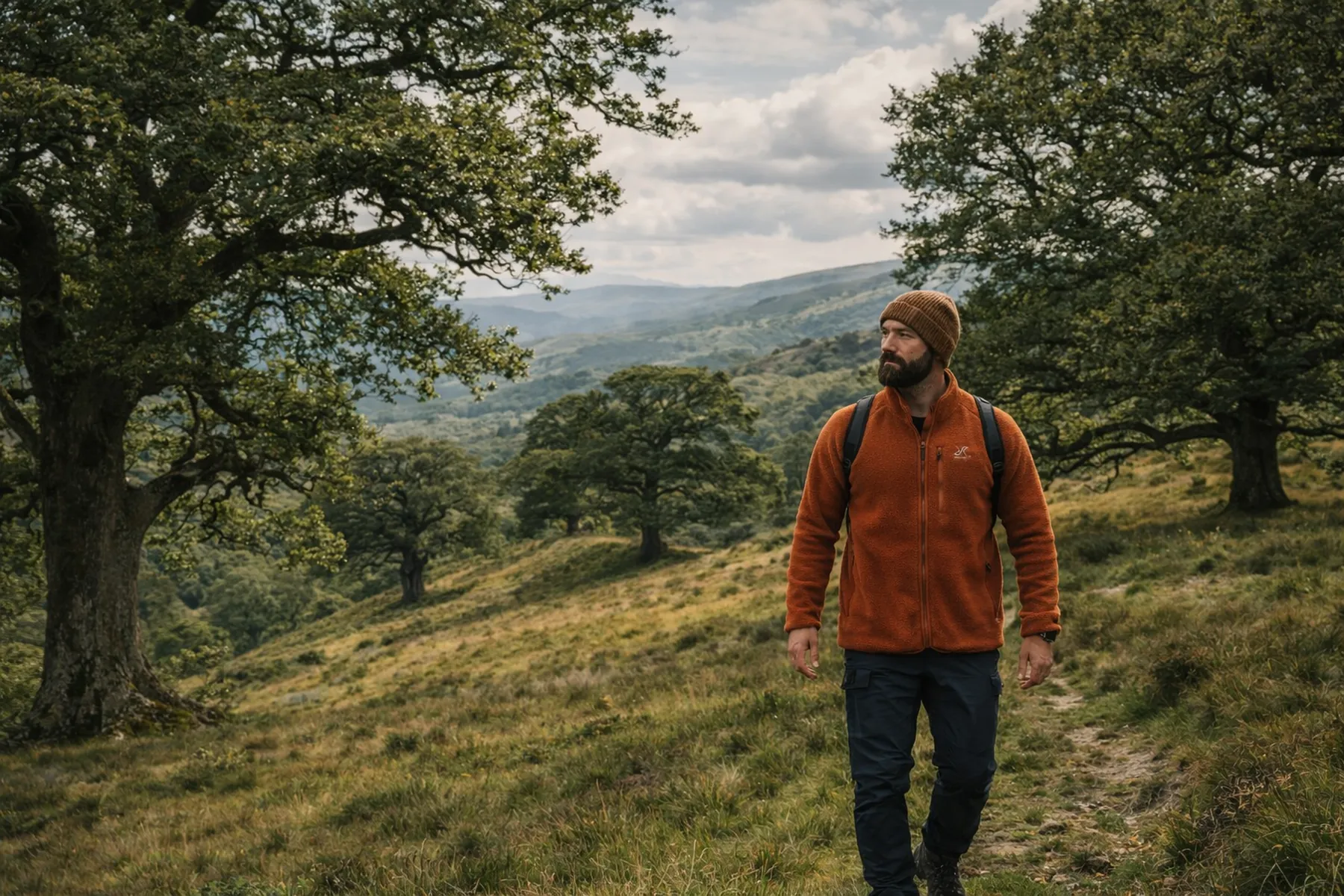 Vandrare i orange Canyon fleecejacka från RevolutionRace i öppet kuperat landskap med ekar