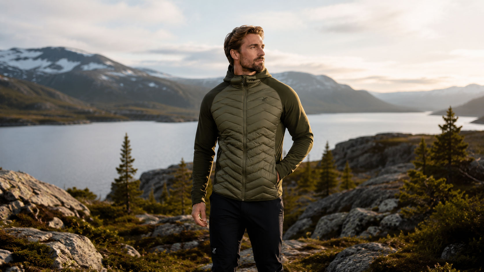 Man i RevolutionRace Evolution Hybrid Fleece Jacket står i bergig naturmiljö vid sjö under kvällsljus.